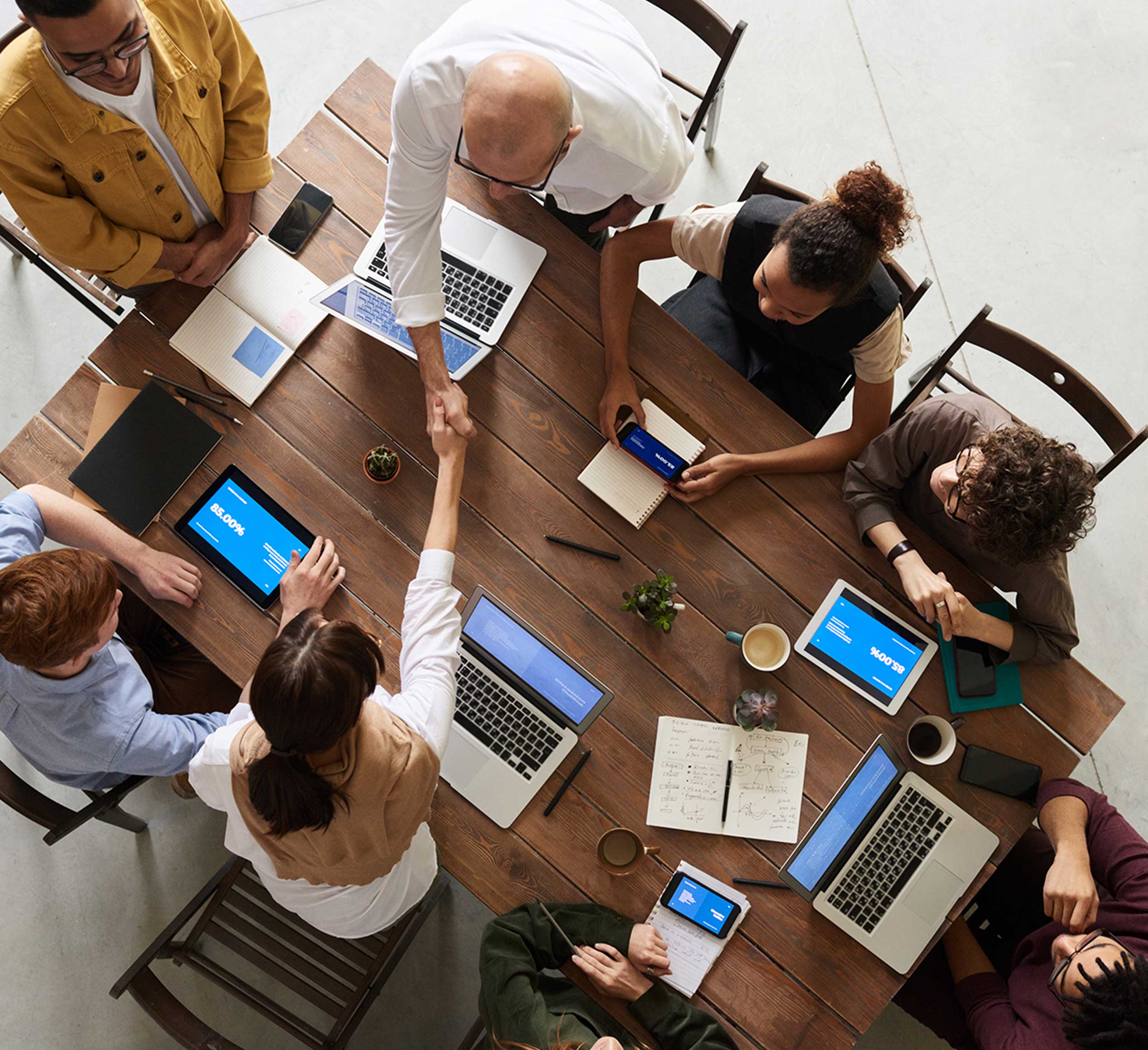 Colaboración Estratégica de Marketing Grupo de profesionales reunidos en una mesa de trabajo, compartiendo ideas y estrechando manos en un entorno colaborativo de marketing y negocios.