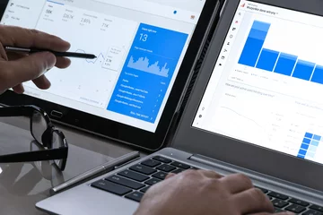 Persona analizando datos en dos pantallas, con gráficos y estadísticas en una laptop y una tablet